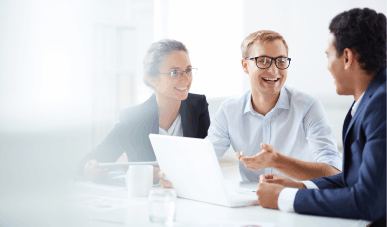 Trois professionnels en réunion, souriants et en pleine discussion autour d’un ordinateur portable, illustrant la collaboration sur les enjeux liés aux données à caractère personnel.