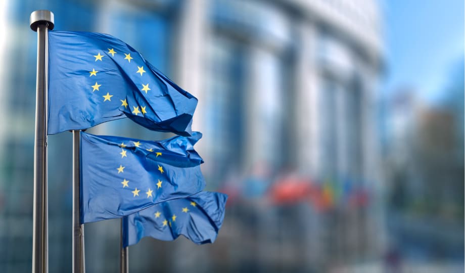 Directive Dora: Drapeaux de l’Union européenne devant un bâtiment institutionnel, représentant le cadre européen du Digital Operational Resilience Act (DORA) et sa mise en conformité harmonisée.